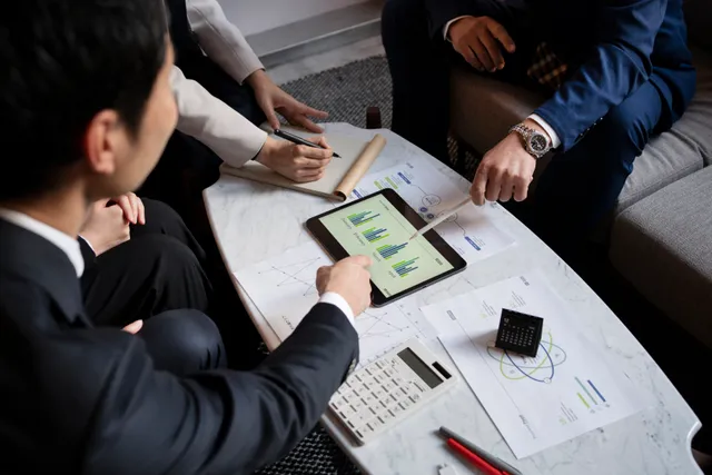 Tiga orang menelaah grafik laporan keuangan di layar tablet